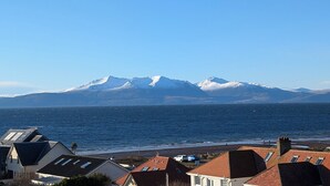 A coastal town with houses, a beach, and snow-capped mountains in the background.