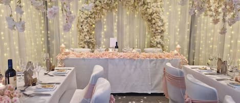 A wedding reception area with tables set for guests, floral decorations, and string lights.