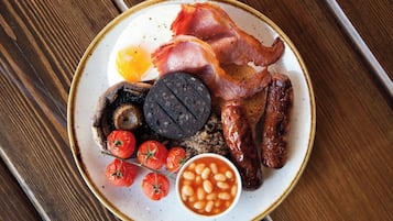 A plate of breakfast food including bacon, sausages, eggs, tomatoes, and beans.