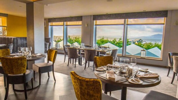A restaurant with tables set for dining, large windows offering a view of greenery and mountains, and a modern interior design.