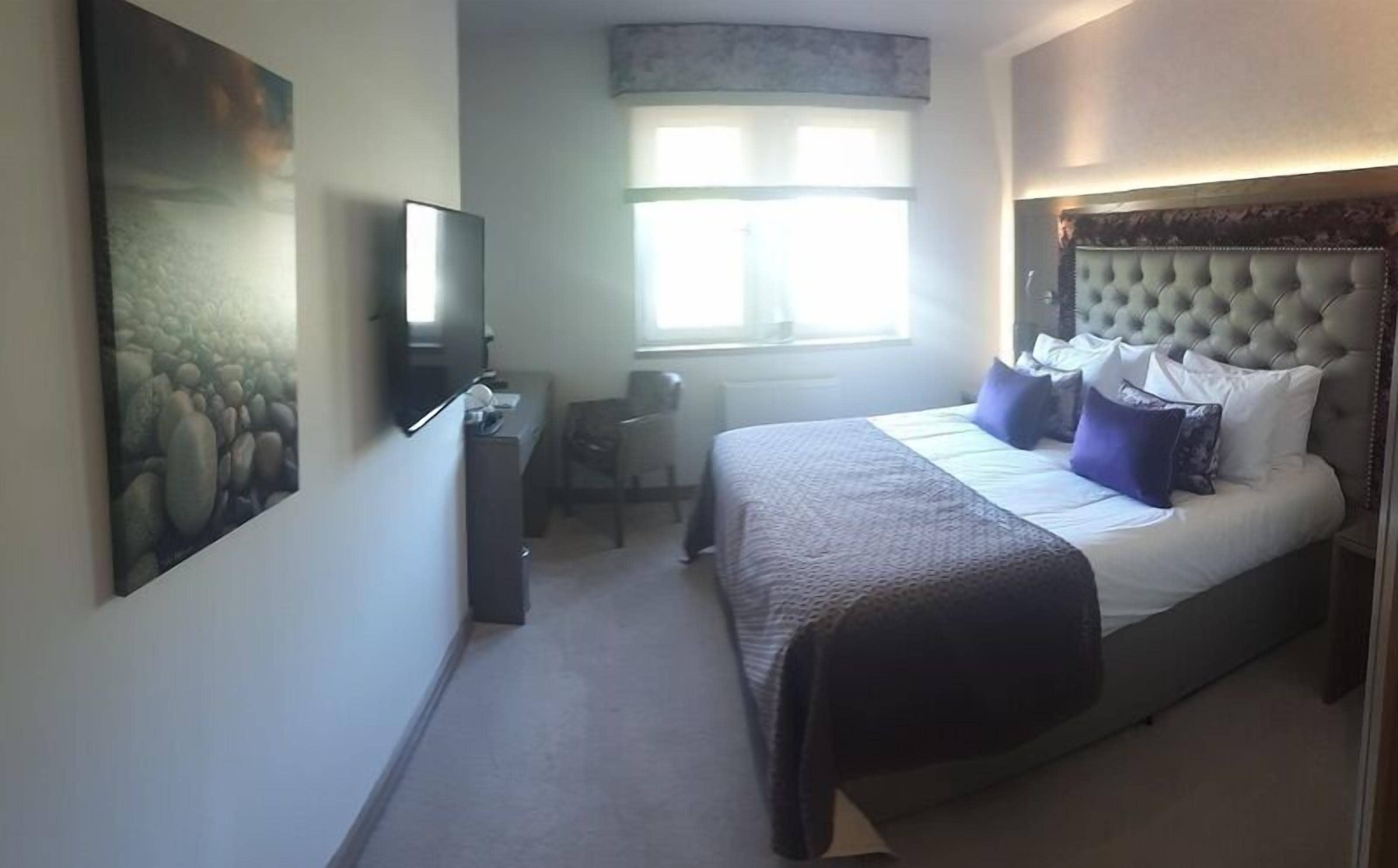 A bedroom with a bed, a desk, a chair, a television, and a window.