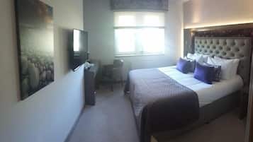 A bedroom with a bed, a desk, a chair, a television, and a window.