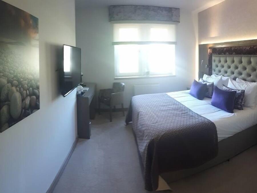 A bedroom with a bed, a desk, a chair, a television, and a window.
