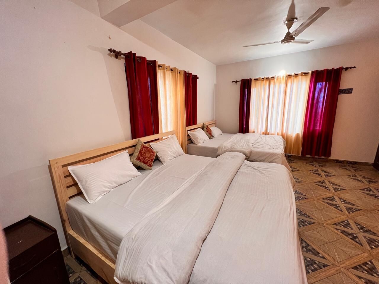 Une chambre d’hôtel avec trois lits, des têtes de lit en bois et des rideaux rouges.
