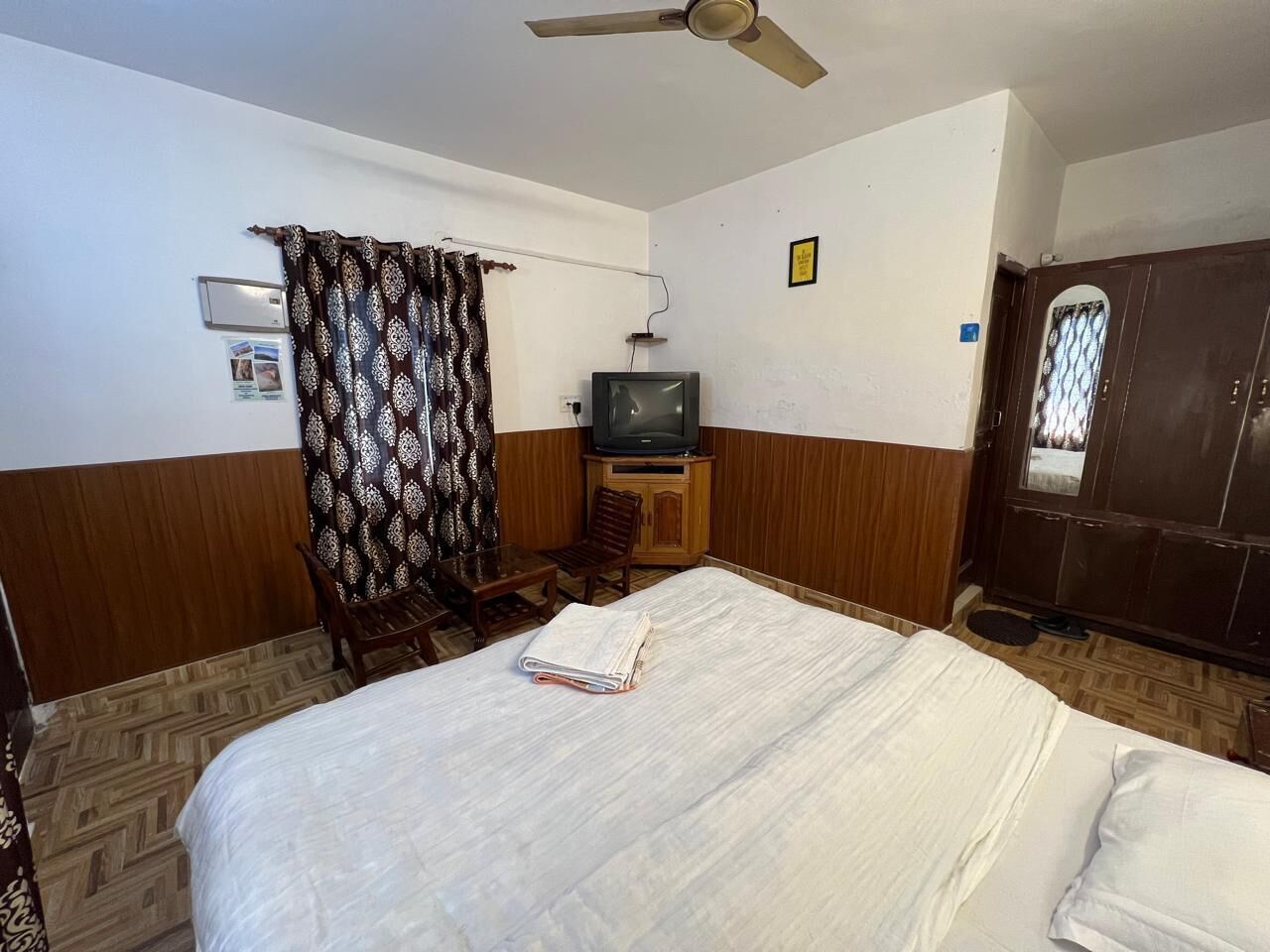Habitación de hotel con cama, televisor, aparador de madera, una silla y una cortina.