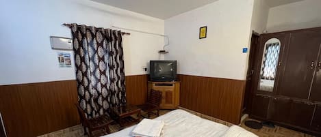 Habitación de hotel con cama, televisor, aparador de madera, una silla y una cortina.