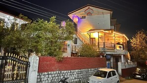 A two-story house with a balcony, a gated entrance, and a parked car. - Uday Homestay (Baijnath)