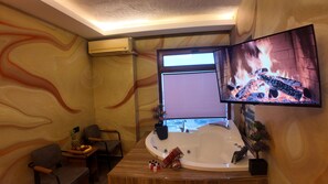 Una habitación con un ventanal grande, chimenea, televisor, bañera y zona de comedor.
