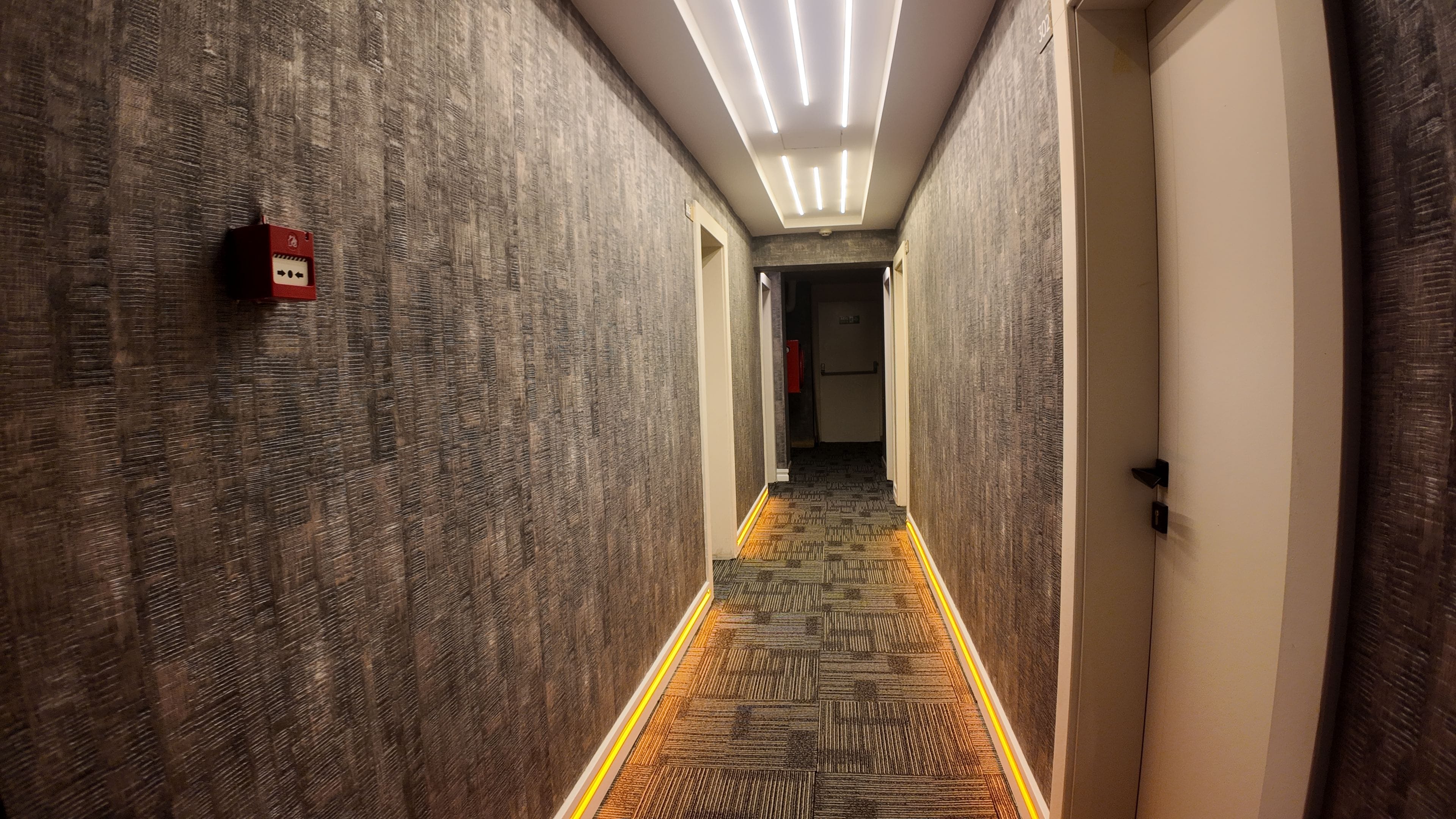 A hallway with patterned walls, a carpeted floor, and a ceiling with linear lighting.