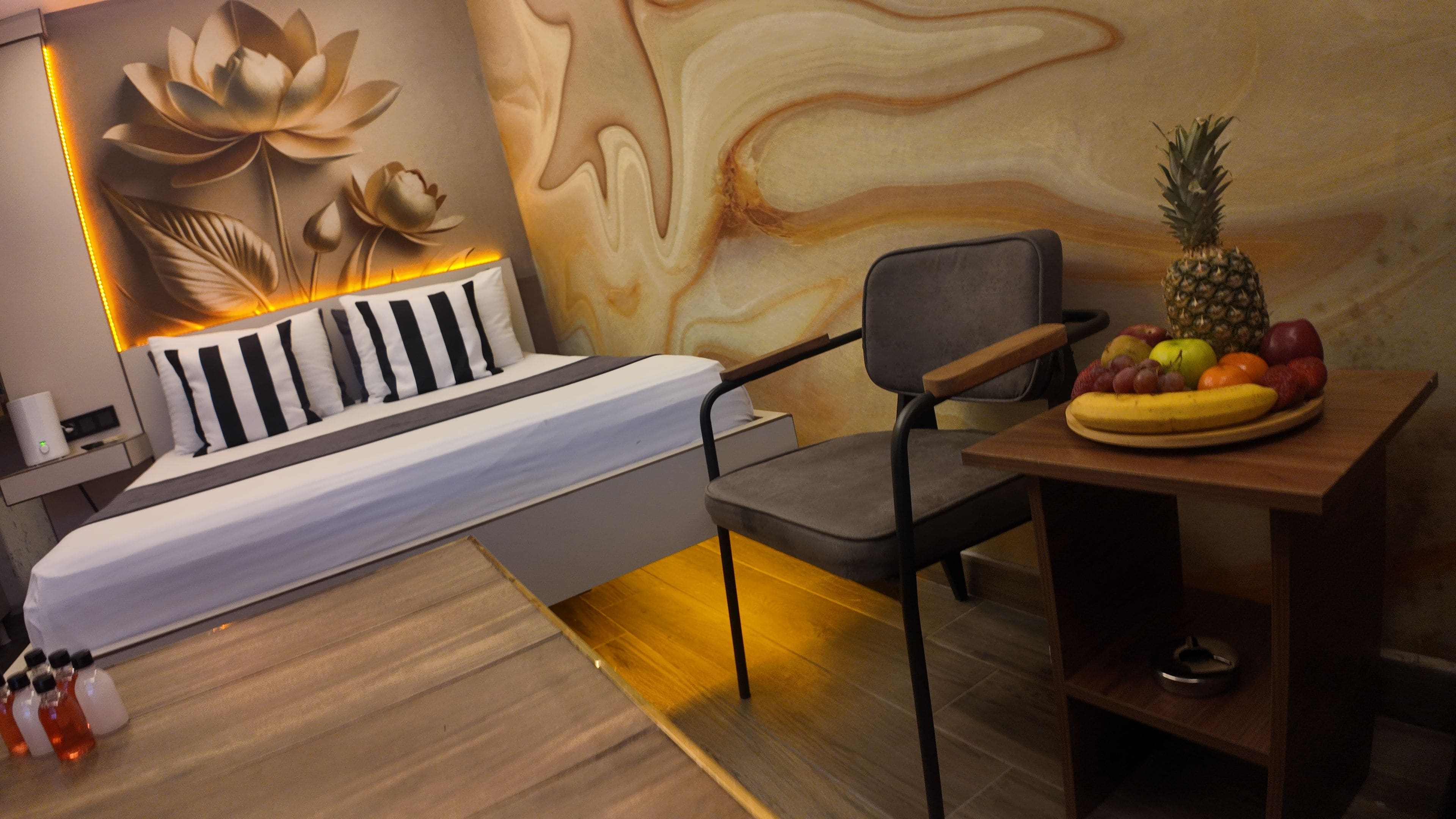 Une chambre à coucher moderne avec un lit, une chaise, une table avec des fruits et un mur orné d’un motif floral.