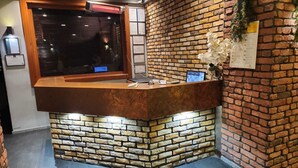 A reception desk with a stone base, a wooden counter, and a window with blinds. - Martin City Hotel (Bursa)