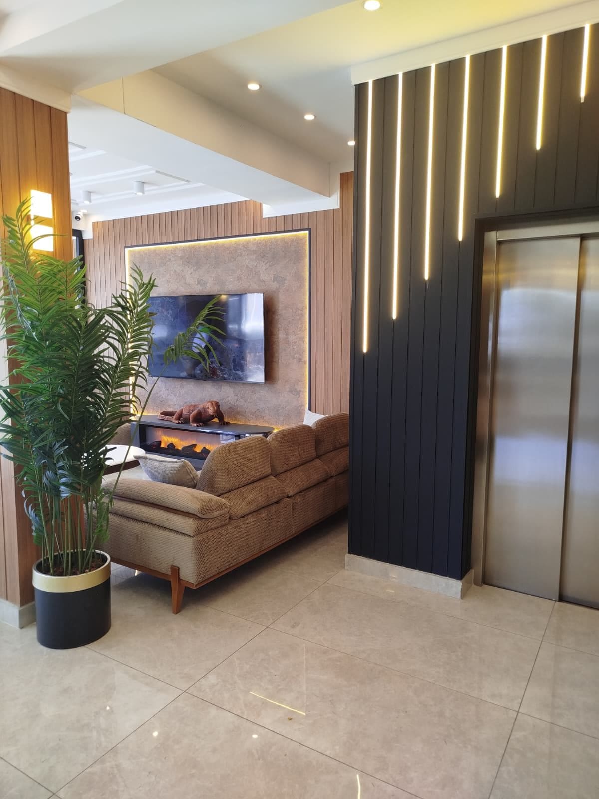 Un espace de vie moderne comprenant un canapé, un grand téléviseur à écran plat, une plante en pot et un luminaire fixé au mur.