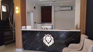 Zona de recepción de un hotel con mostrador de mármol, candelabro, mostrador de recepción y una escalera.