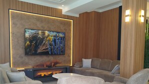 Una sala moderna con televisión de pantalla plana montada en una pared de madera, chimenea y un área de descanso con sofás y sillones.