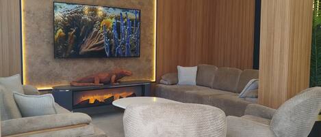 Una sala de estar moderna con un televisor de pantalla plana montado en una pared de madera, una chimenea y un área de estar con sofás y sillones.