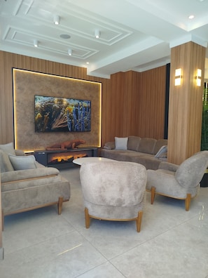 A modern living room with a flat-screen TV mounted on a wooden wall, a fireplace, and a seating area with sofas and armchairs. - Martin City Hotel (Bursa)