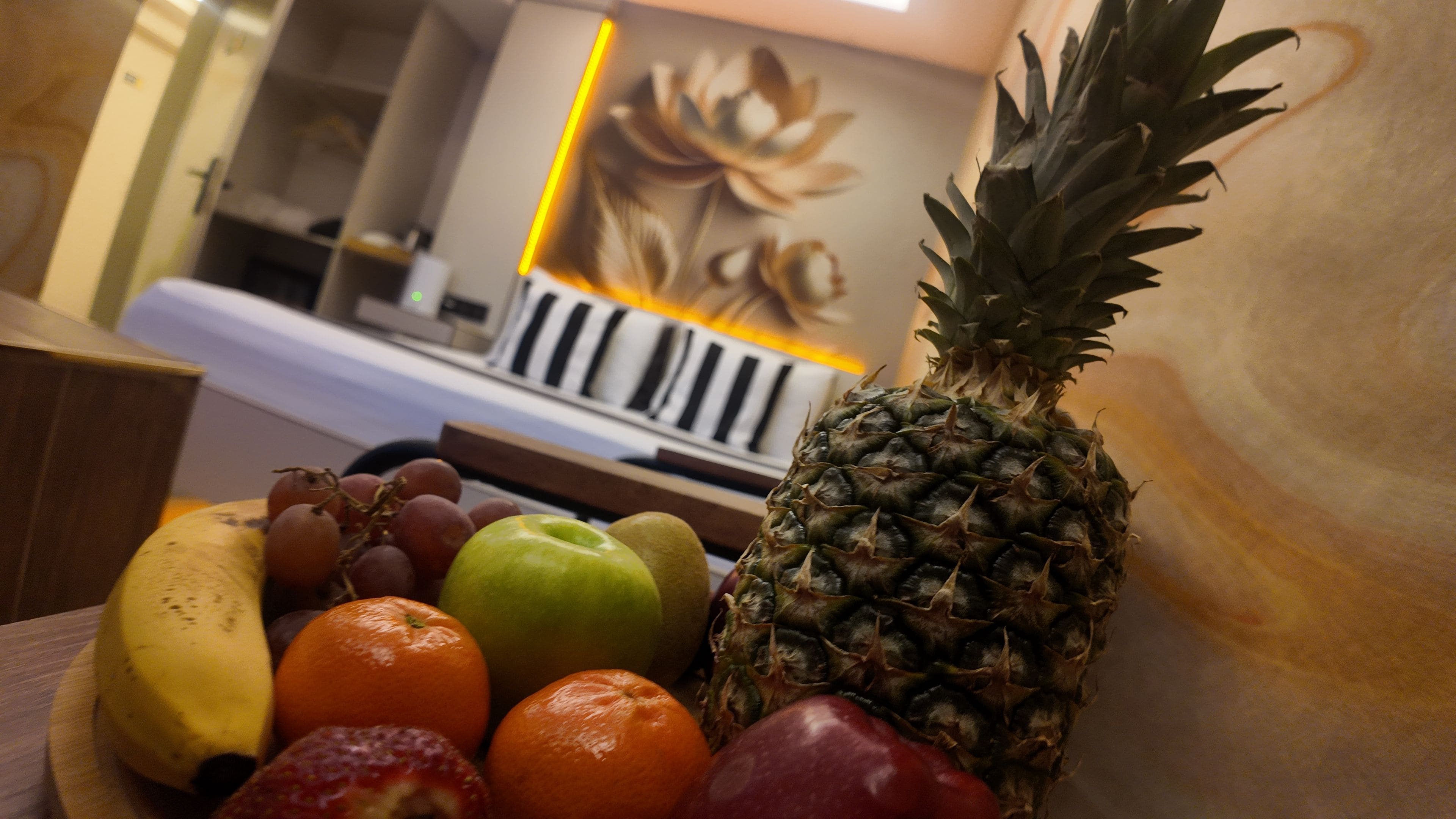 A fruit bowl with a pineapple, grapes, an apple, and a banana on a wooden surface.