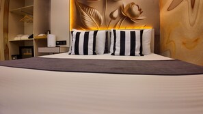 A hotel room with a bed, pillows, a bedside table, a lamp, a wardrobe, and a wall with a floral design. - Martin City Hotel (Bursa)