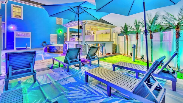 A poolside area with lounge chairs and umbrellas, a covered seating area, and a view of the pool and surrounding greenery.