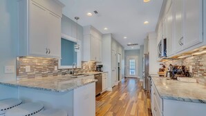 A modern kitchen with white cabinets, a marble countertop, and a wooden floor.