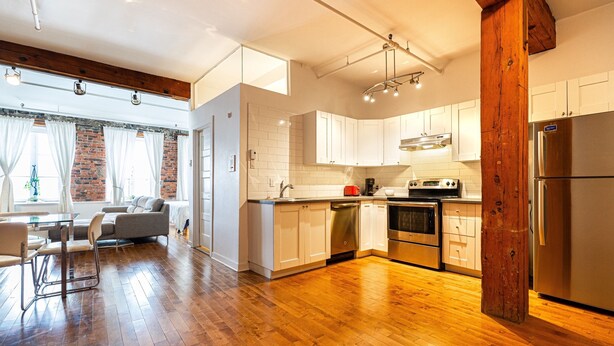 A modern kitchen with wooden flooring, white cabinets, and stainless steel appliances. - Adorable Loft in the Old Montreal  (Montreal)