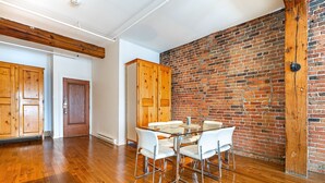 A dining area with a glass table and white chairs, a brick wall, wooden cabinets, and a wooden ceiling beam. - Adorable Loft in the Old Montreal  (Montreal)