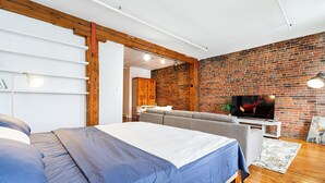 A modern bedroom with a large bed, a grey sofa, a TV, and a brick wall. - Adorable Loft in the Old Montreal  (Montreal)