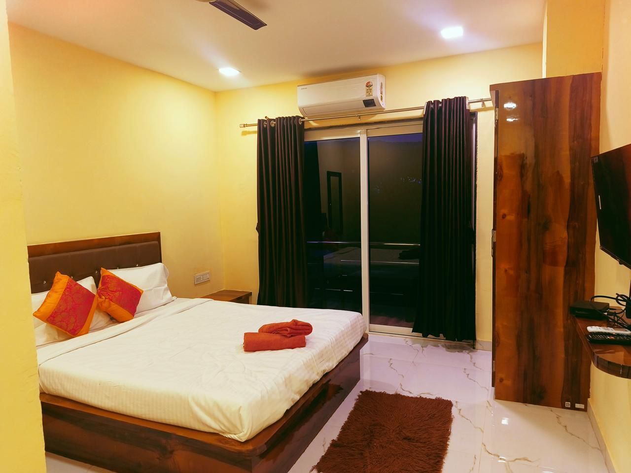 A hotel room with a bed, a TV, a wooden door, and a window with curtains.