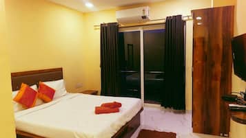 A hotel room with a bed, a TV, a wooden door, and a window with curtains.