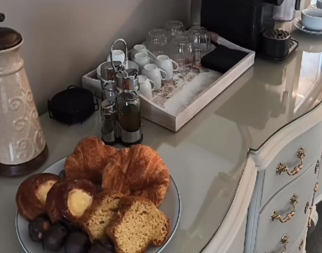 Un safata d'esmorzar amb croissants, pa i baies en un plat, una cafetera i una safata plena de tasses i gots.