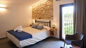 Un dormitorio con cama, mesita de noche, una silla y vistas al verde exterior.