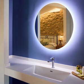 Une salle de bain avec un miroir rond, un lavabo blanc et un mur texturé derrière le miroir.