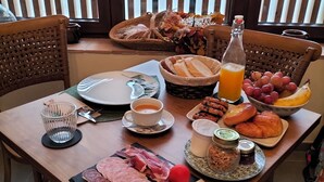 Una mesa de desayuno con diversos alimentos, como pan, bollería, queso y una botella de zumo de naranja.