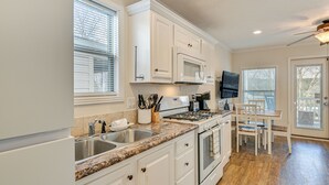 Una cocina con armarios blancos, encimera de granito, microondas, estufa, fregadero y comedor con mesa y sillas.