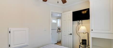 A bedroom with a bed, a ceiling fan, a TV, and a lamp.