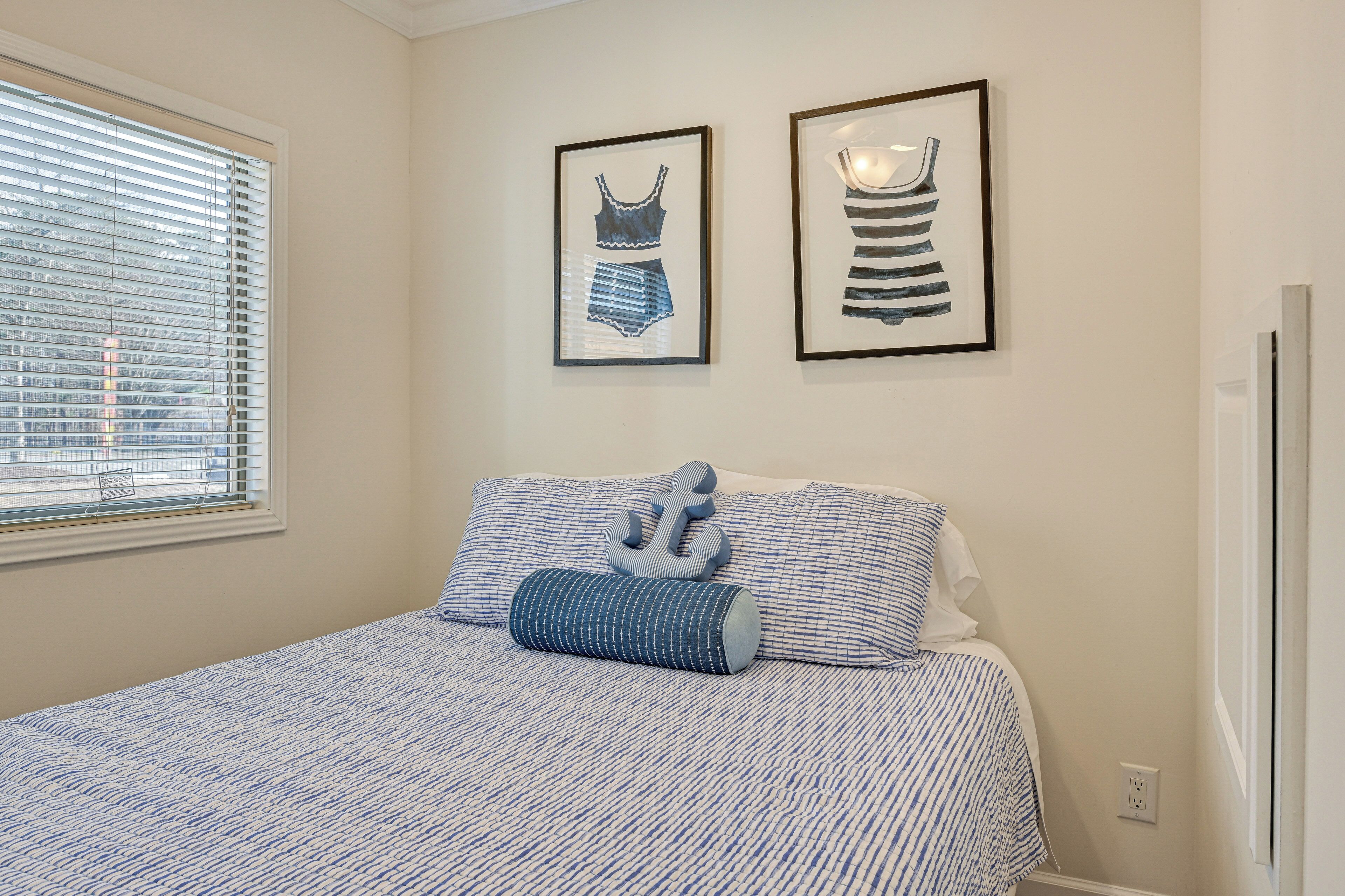 A bedroom with a bed, a window with blinds, and two framed pictures on the wall.