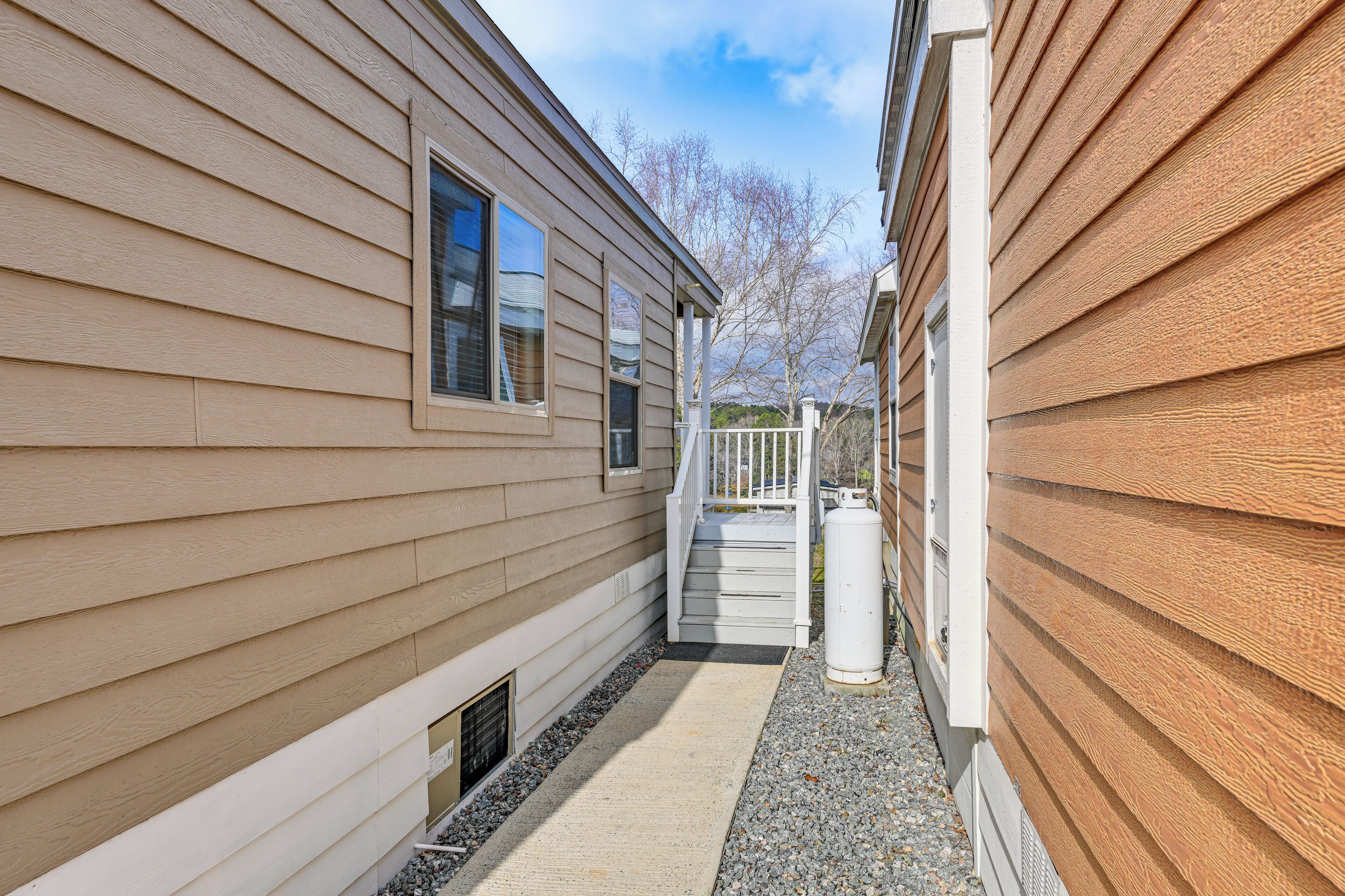Un étroit sentier mène à une maison en bois avec une porte d’entrée blanche et un petit porche.
