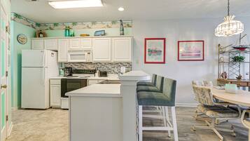 A kitchen with white cabinets, a refrigerator, a microwave, and a sink. There is a dining area with a table and chairs.