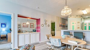 Une cuisine moderne avec des meubles blancs, un coin repas doté d’une table ronde et de chaises, et un salon avec un canapé.