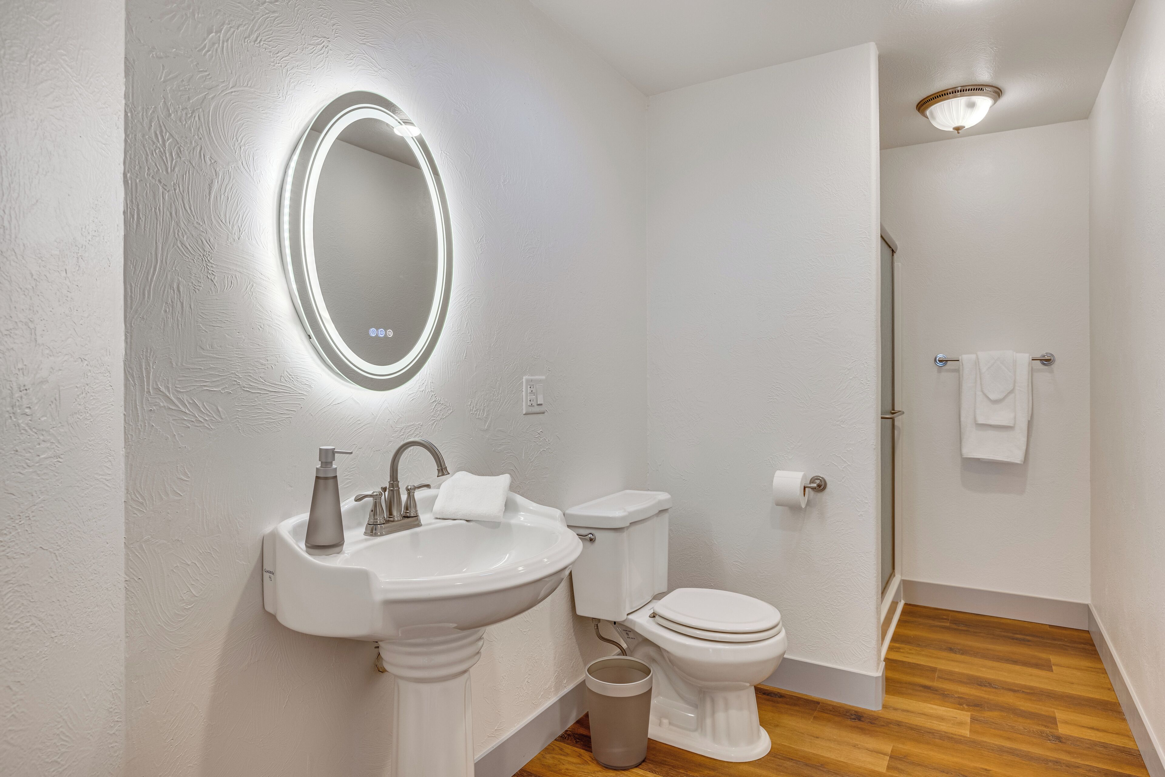 Un bagno con un lavandino su piedistallo, un water e uno specchio illuminato.