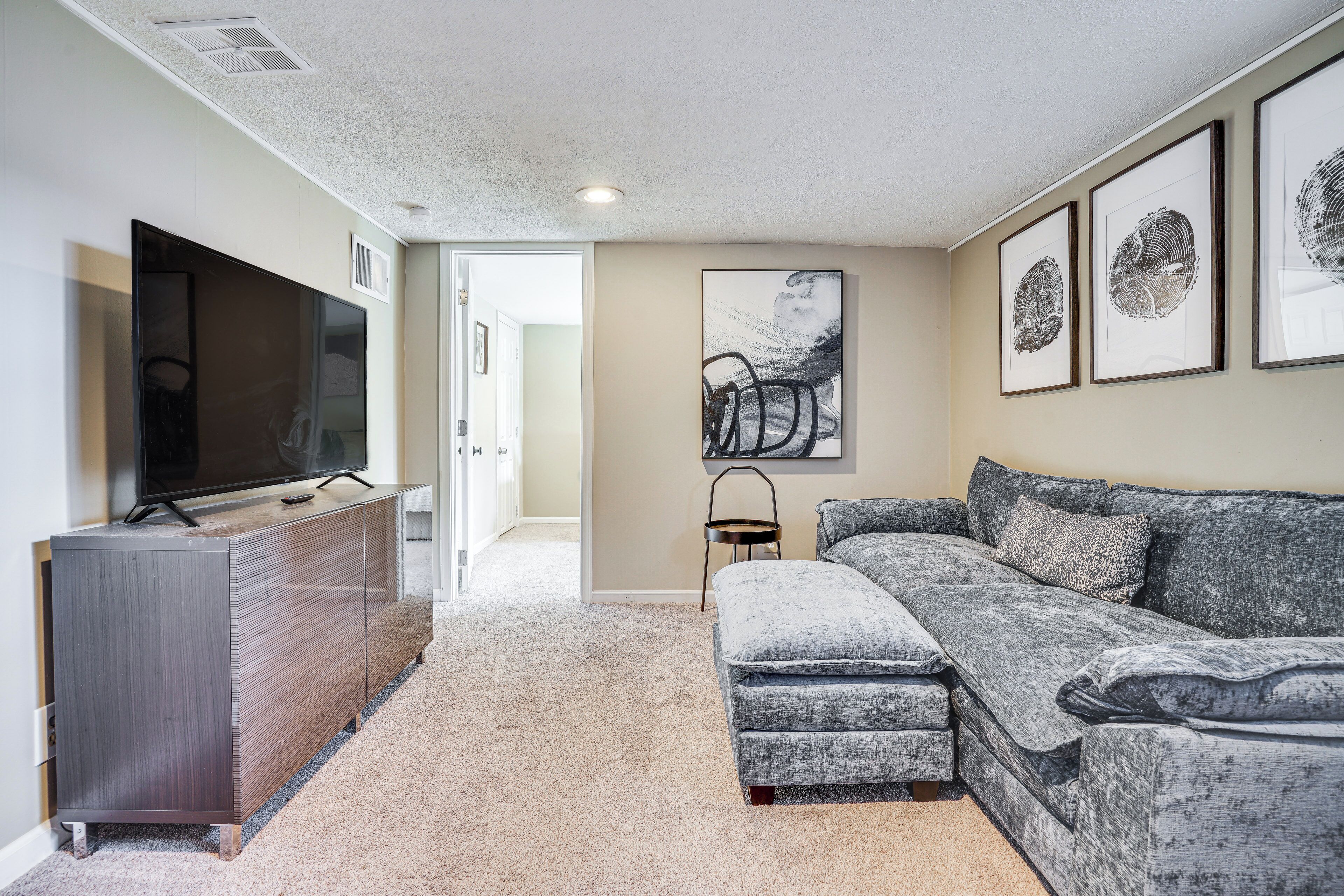 A modern living room with a flat-screen TV, grey sectional sofa, and a wooden cabinet.
