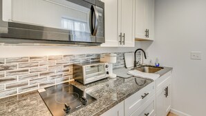 A modern kitchen with white cabinets, a stainless steel microwave, a built-in toaster oven, and a granite countertop. - Studio Apartment Near East Atlanta Village (Atlanta)
