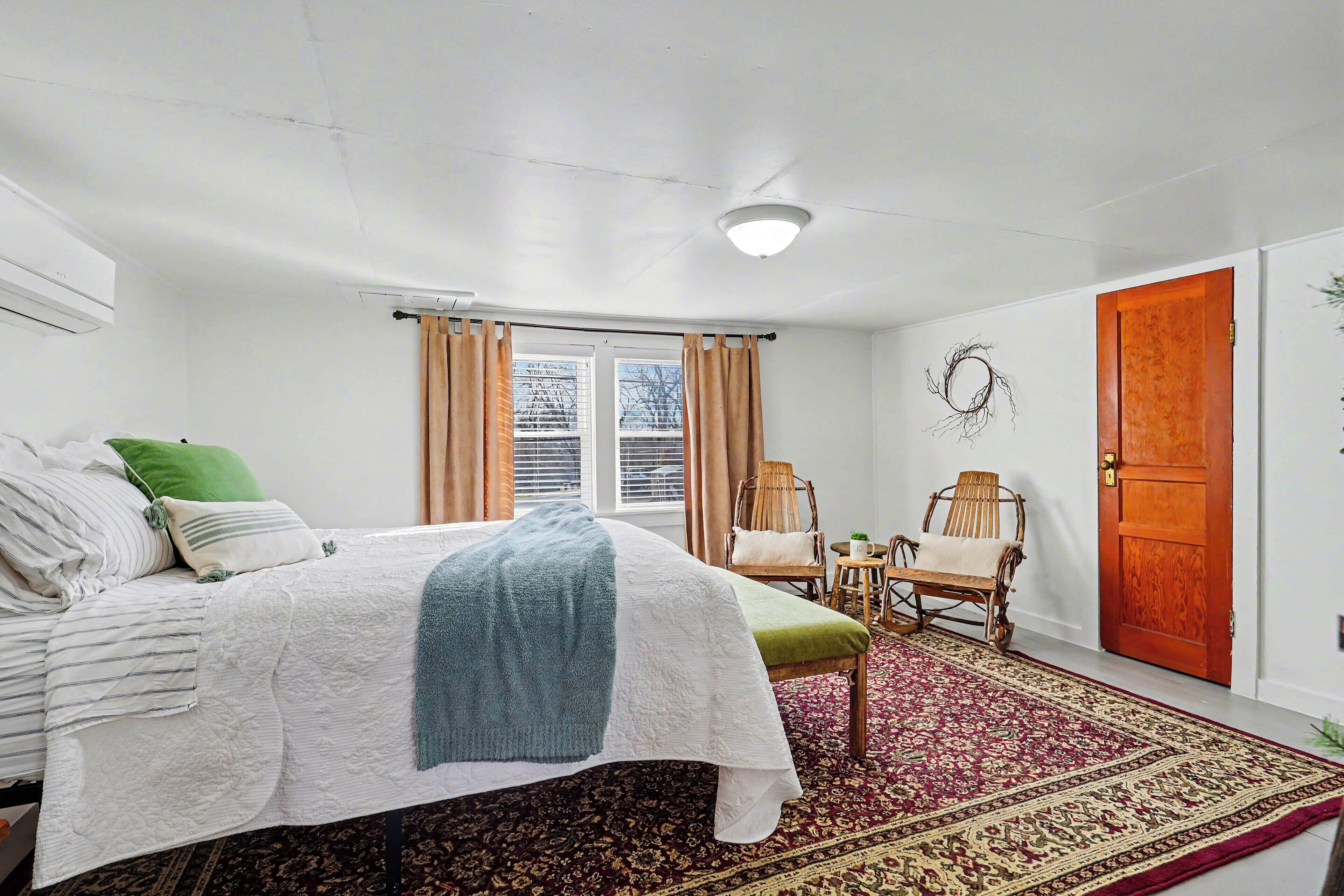 A bedroom with a bed, a chair, a rug, a door, and a window.