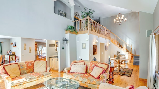 A spacious living area with a high ceiling, a wooden staircase, and a glass coffee table.