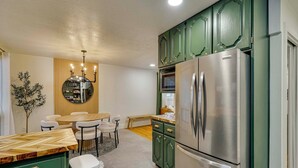 Eine moderne Küche mit grünen Schränken, einem Edelstahlkühlschrank, einem Essbereich mit rundem Tisch und Stühlen sowie einem dekorativen Spiegel über dem Tisch.