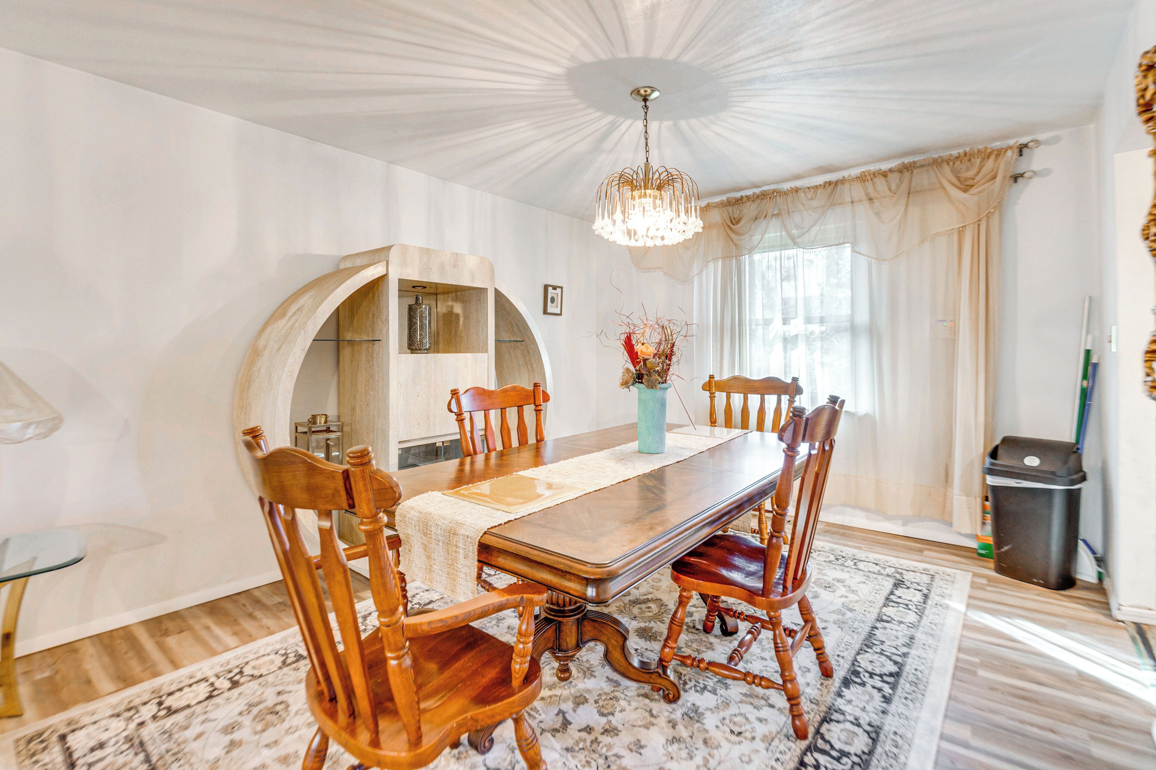Una sala da pranzo con tavolo in legno, sedie, un lampadario e un'ampia finestra con tende.
