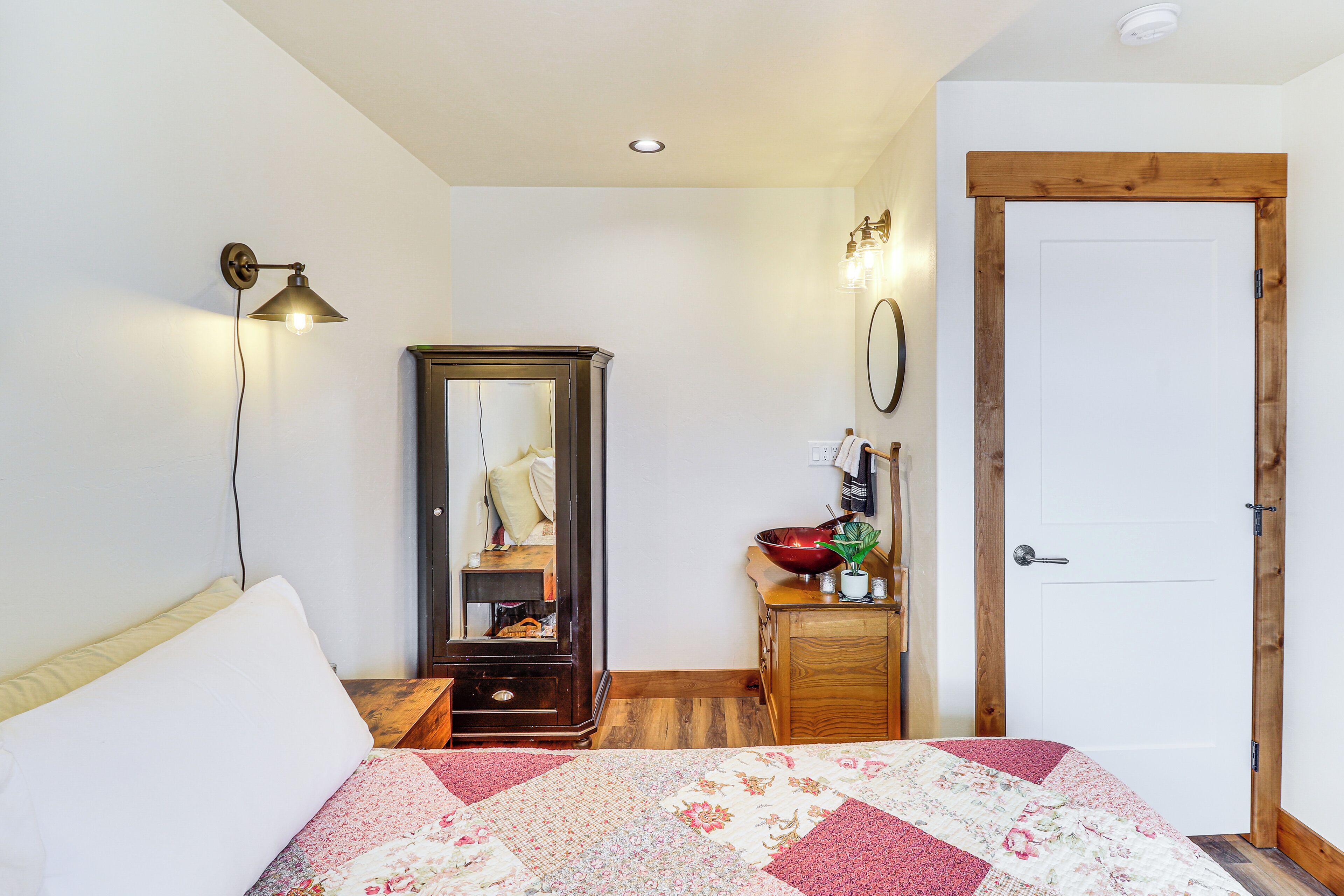 Un dormitorio con cama, cómoda, espejo, lámpara y una puerta.