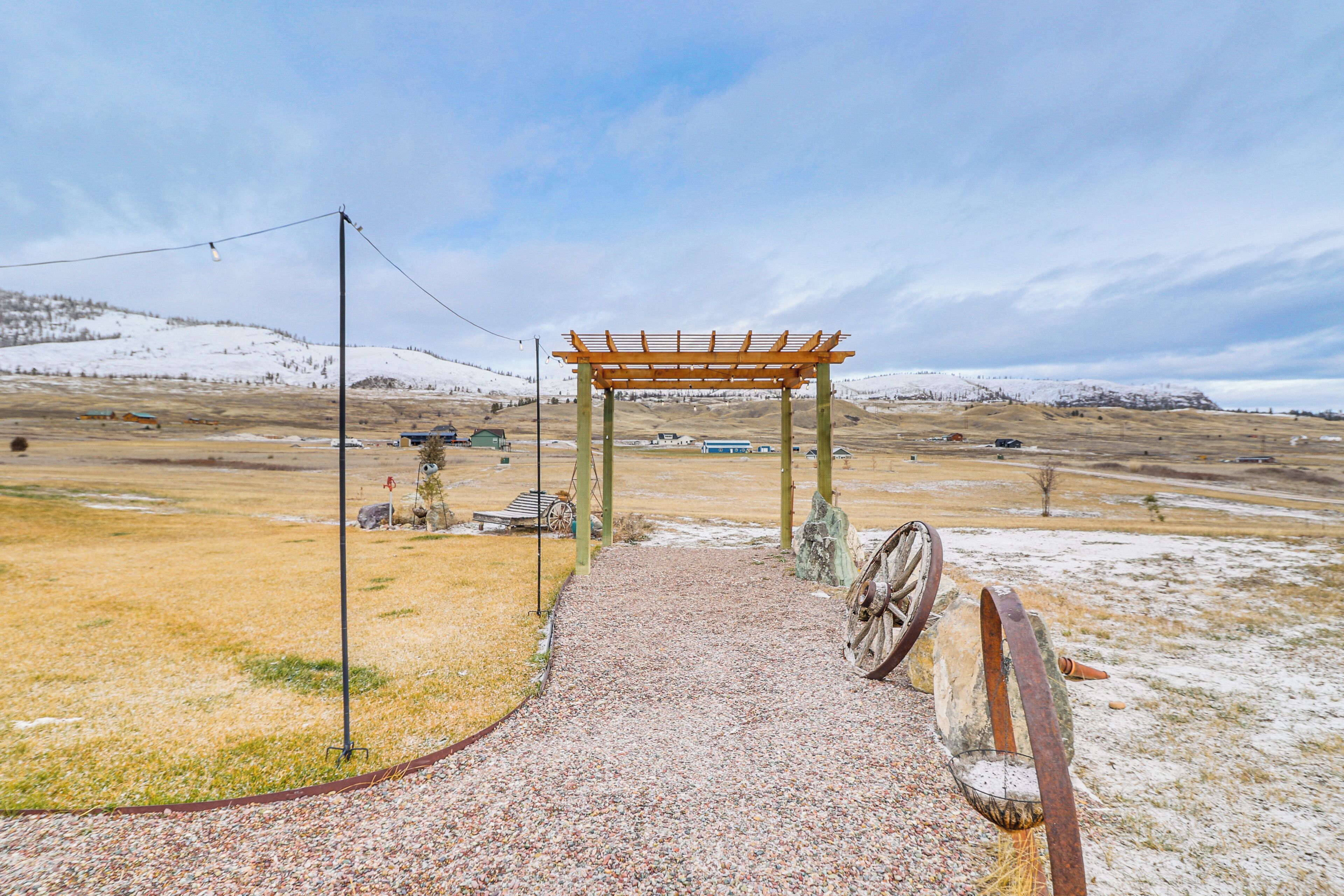 A gravel path leading to a wooden pergola in a rural setting with snow-covered hills in the background.