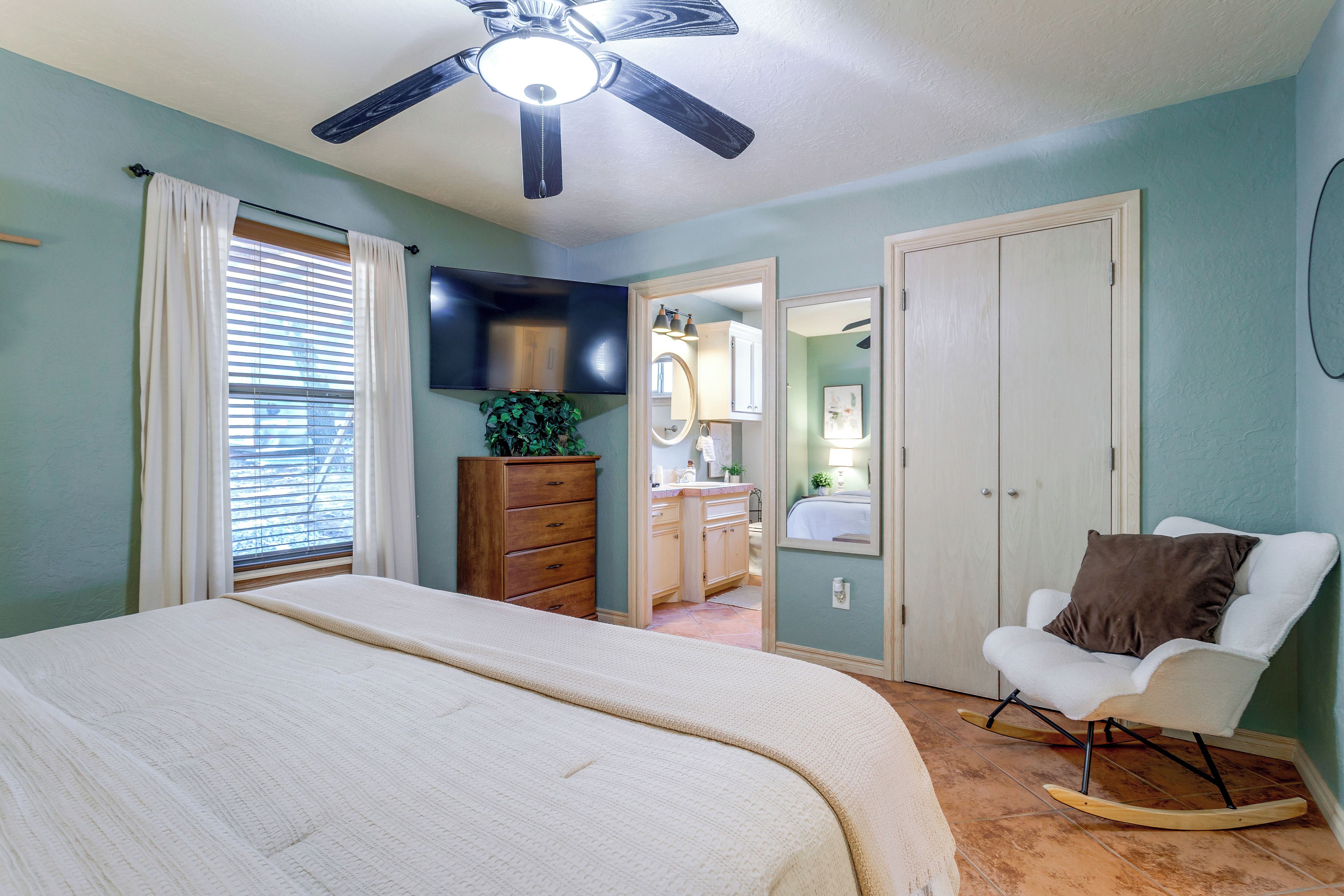 Une chambre à coucher avec un lit, une chaise, une commode, un téléviseur et un ventilateur de plafond.