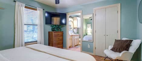 A bedroom with a bed, a chair, a dresser, a TV, and a ceiling fan.